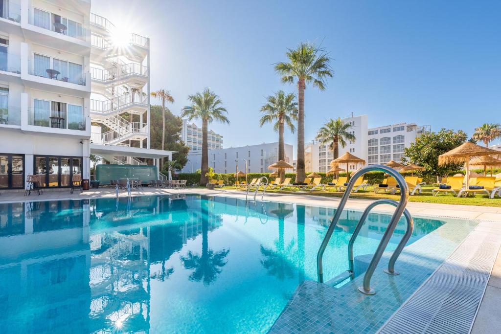 Viesnīcas baseins ar skatu uz palmām un sauļošanās krēsliem, saulains laiks un moderna arhitektūra. Ideāla vieta atpūtai un relaksācijai.