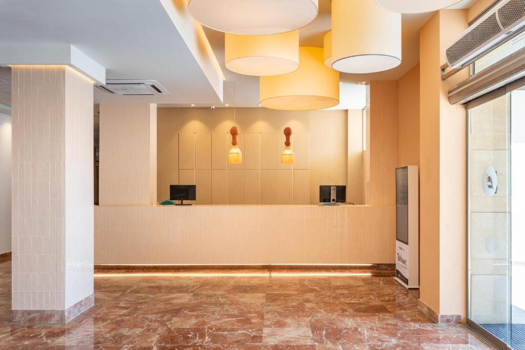 Mūsdienīga viesnīcas reģistratūra ar gaišām krāsām un elegantu apgaismojumu. Interjerā ir marmora grīda un stilīgas lampas, kas rada siltu atmosfēru.