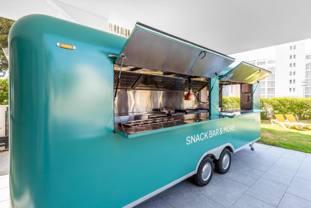 Zaļš uzkodu piegādes kamionu ar atvērtām durvīm un grila aprīkojumu, kas atrodas dārzā blakus viesnīcai. 