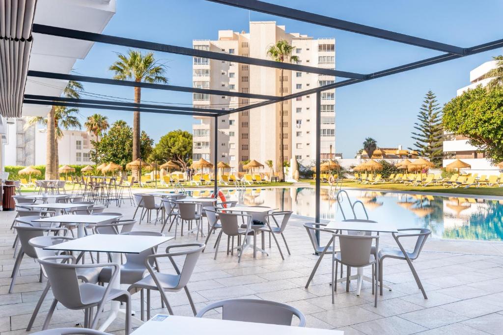 Peldbaseins ar sauļošanās krēsliem un palmām, redzams no terases ar baltām galdiem un krēsliem. Ideāla vieta atpūtai un relaksācijai.