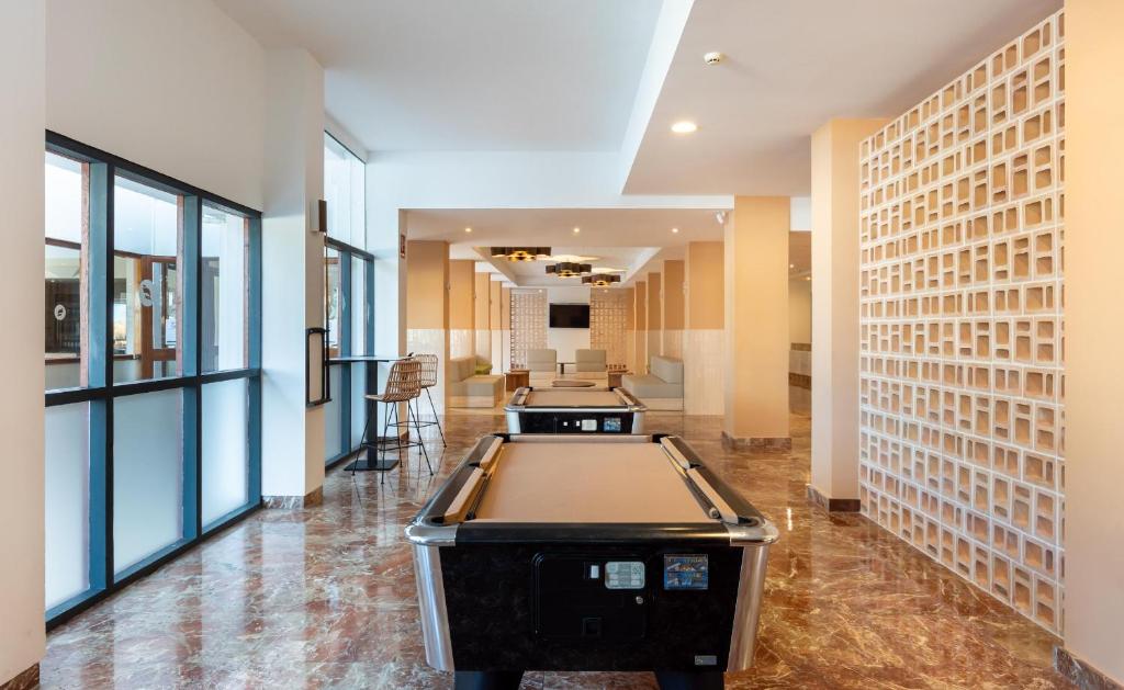 Mūsdienīgs un gaišs interjers ar biljarda galdu, kas atrodas plašā telpā ar lieliem logiem un modernām apdares elementiem.