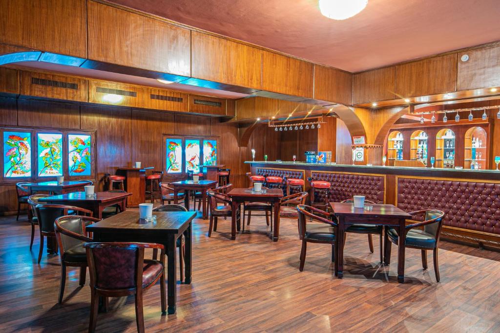 Elegantā bāra interjers ar koka apdari un krāsainiem logiem, kas piešķir siltu atmosfēru. Galdi un krēsli ir izvietoti visā telpā, radot patīkamu vidi atpūtai.