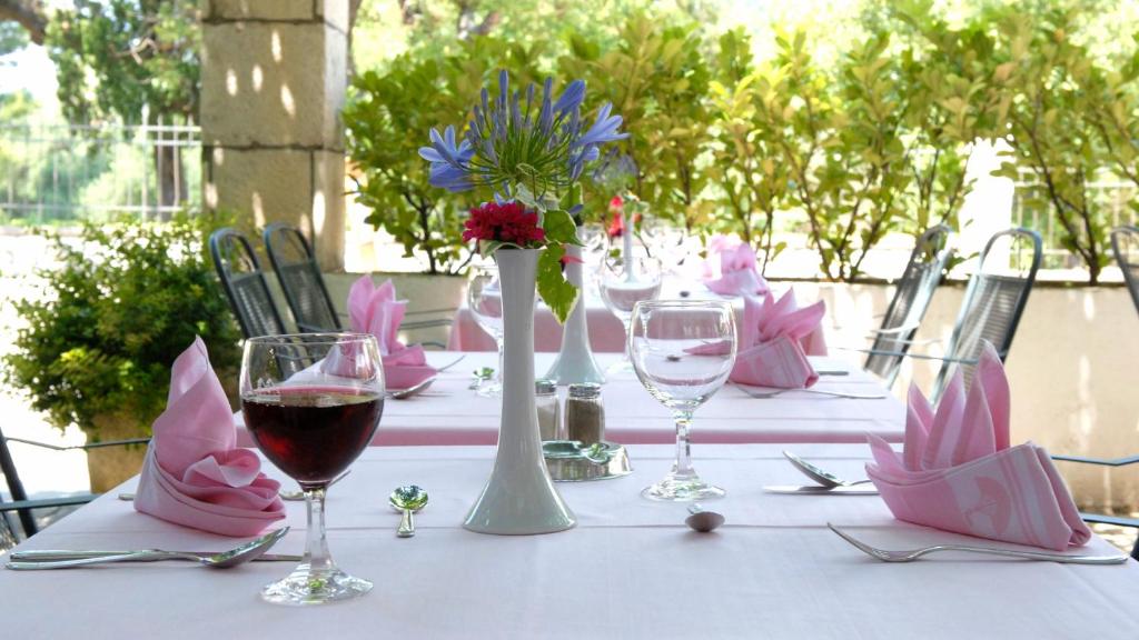 Eleganti iekārtota galda kompozīcija ar rozā salvetēm un ziedu kompozīciju centrā, radot draudzīgu un svinīgu atmosfēru. Galda piederumi un glāzes ir rūpīgi sakārtoti, piedāvājot aicinošu skatu uz āra ēdamzāli.