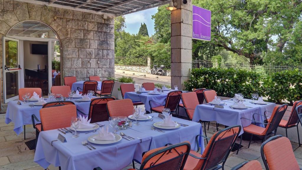 Āra restorāna terase ar galdiem, kas klāti ar ziliem galdautiem un oranžām krēslām, apzaļumots fons un viesmīlīgs atmosfēra. Atpūtas vieta ir ideāla relaksācijai un maltītei.