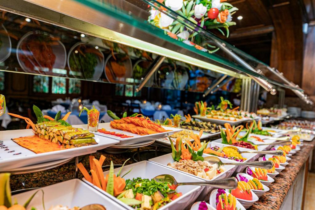 Bagātīgs un krāsains bufetes galds ar dažādiem gardumiem, tostarp dārzeņu un augļu ēdieniem, kas rotāti ar košām garnējumiem. Ideāli piemērots svinībām vai svinīgiem pasākumiem.