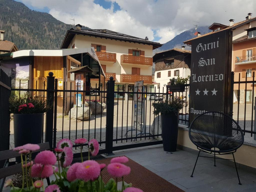 Mājas viesnīcas "Garni San Lorenzo" ieeja ar ziediem priekšplānā un kalnu ainavu fonā.