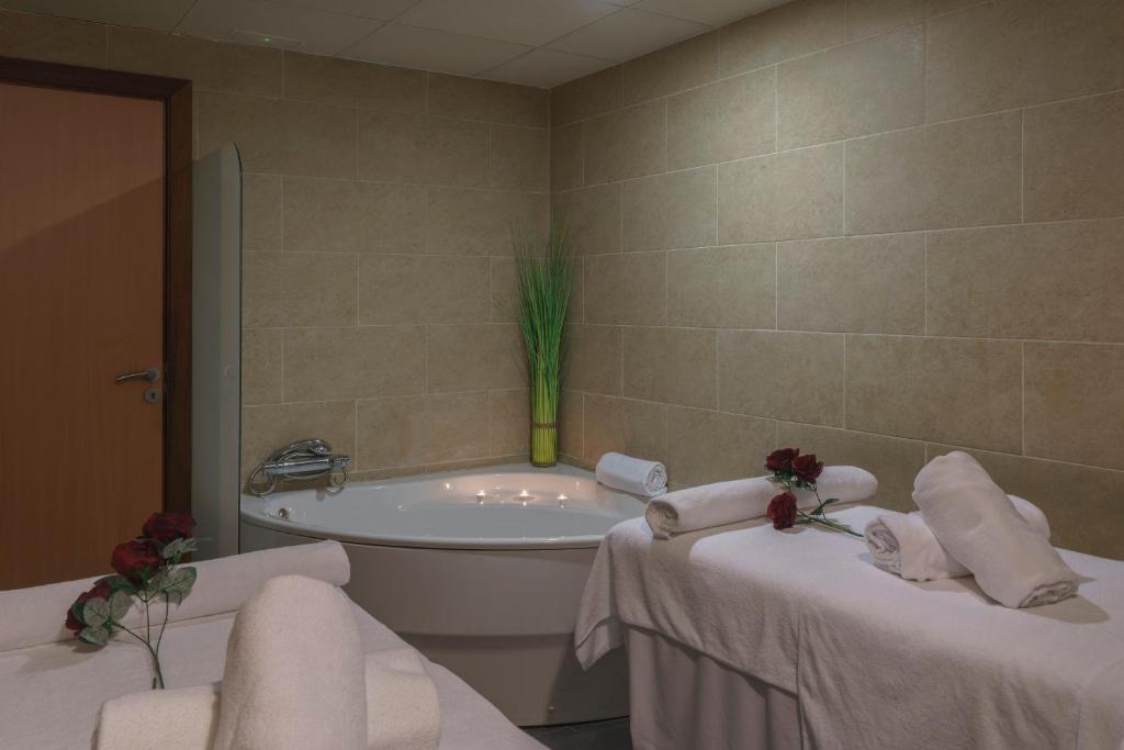 Mūsdienīgs spa telpa ar masāžas galdiem, baltām dvielīšiem un apgaismotu vannu, kas rotāta ar rozēm. Daba un relaksācija apvienotas harmoniskā vidē.