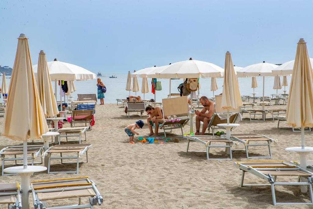 Pludmale ar saulessargiem un atpūtniekiem, bērni spēlējas smilšu kastē. Relaksējoša atmosfēra pie jūras.