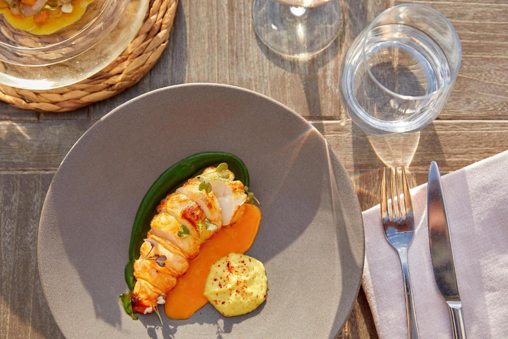 Gurķu salāti ar garnelēm un krabju gaļu uz pelēka šķīvja, pasniegti kopā ar apelsīnu biezeni un zaļo mērci. Elegants galda iestatījums ar ūdens glāzi un sudraba piederumiem.