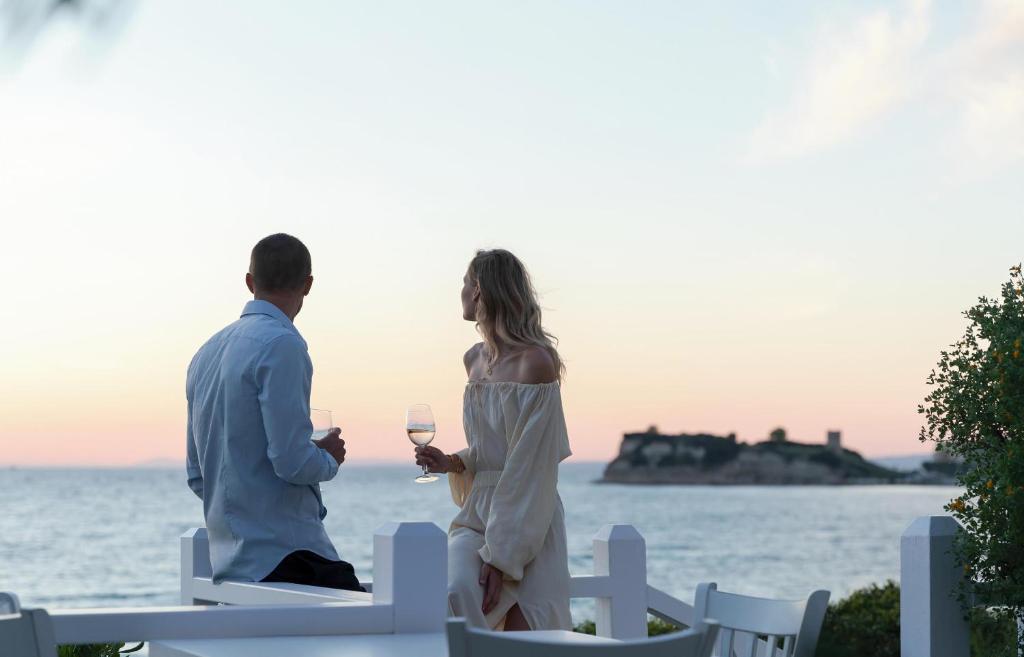 Pāris, baudot vīnu, skatās uz saulrietu pie jūras. Fons veido romantisku atmosfēru ar klusām viļņu skaņām un krāsu spēlēm debesīs.