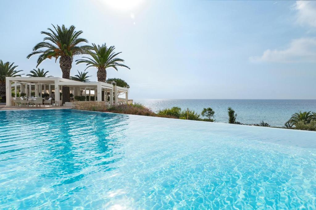 Mūsdienīgs baseins ar skatu uz jūru, apkārt palmām un elegantām ēkām, radot relaksējošu un greznu atmosfēru.