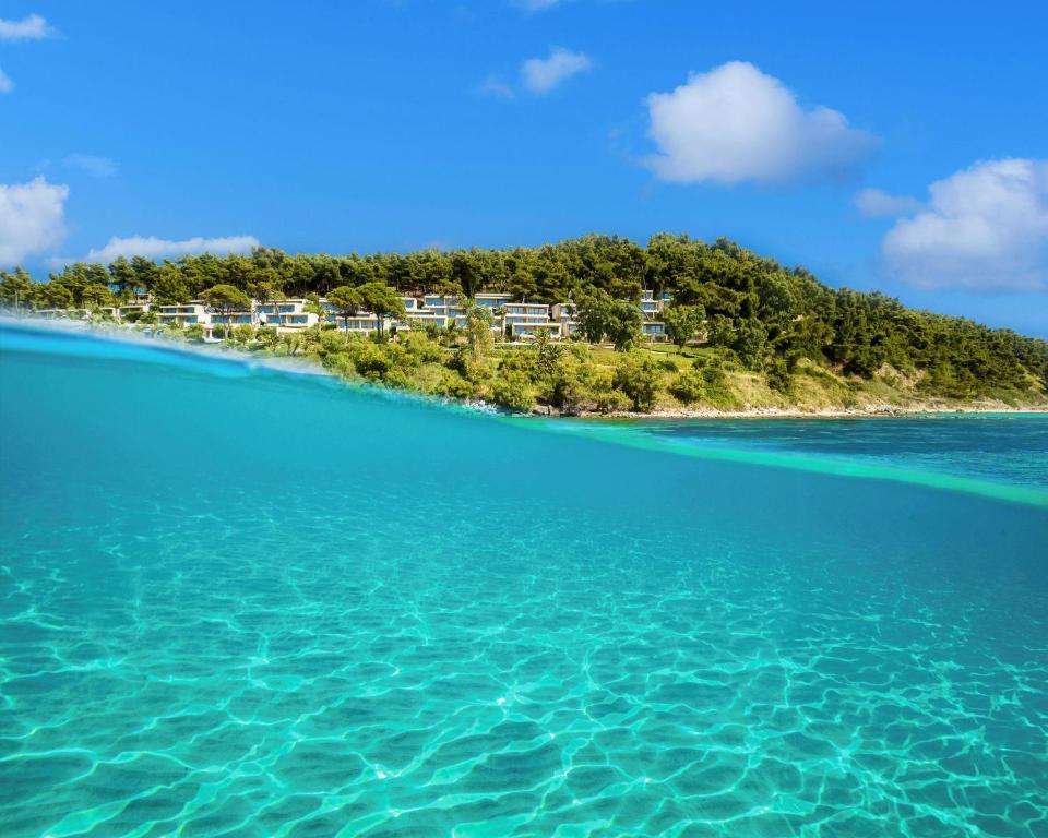 Tīras zilas jūras ūdens un zaļa krasta līnija ar modernām villām. Skaists dabas skats, kas apvieno ūdens un zemes elementus.