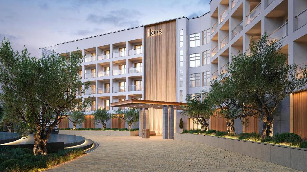 Mūsdienīgs viesnīcas "Ikos" ieejas dizains ar elegantu koka akcentu un apzaļumotu apkārtni. Viesnīca ir izvietota modernā ēkā ar plašiem balkoniem.