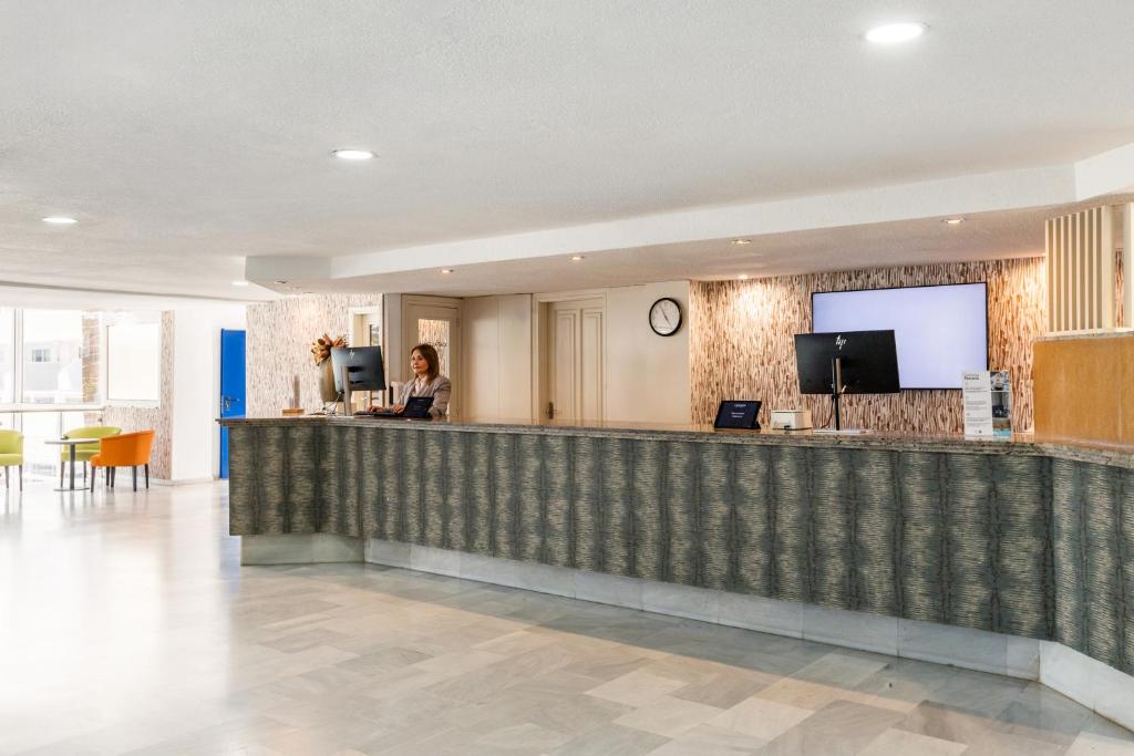 Recepcija modernā viesnīcā ar laipnu darbinieku un mūsdienīgu interjeru. Apskatāmas ērtas sēdvietas un tehnoloģijas.