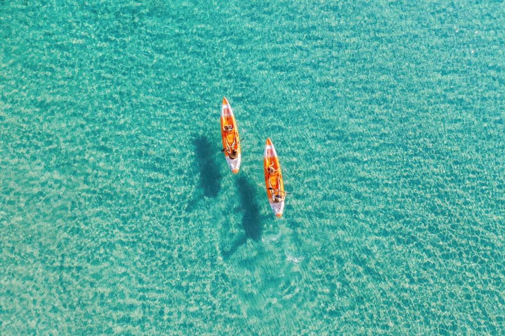 Divi kajaki peld pa kristāldzidru ūdeni, izceļot saulainu dienu un mierīgu atmosfēru.