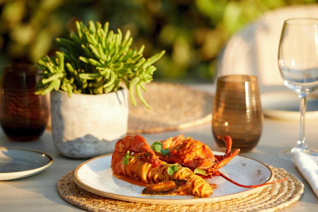 Garšīgi sagatavota lobsta porcija uz šķīvja ar makaronu un garšaugiem, dekorēta ar augu un glāzēm uz galda.