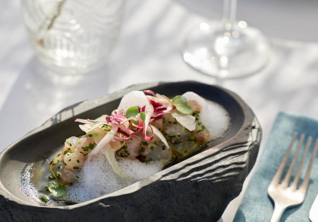 Gourmet ēdiens modernā traukā ar putojošu virsmu, dekorēts ar dārzeņiem un garšaugiem. Elegants pasniegšanas stils ar tradicionālu galda piederumu.