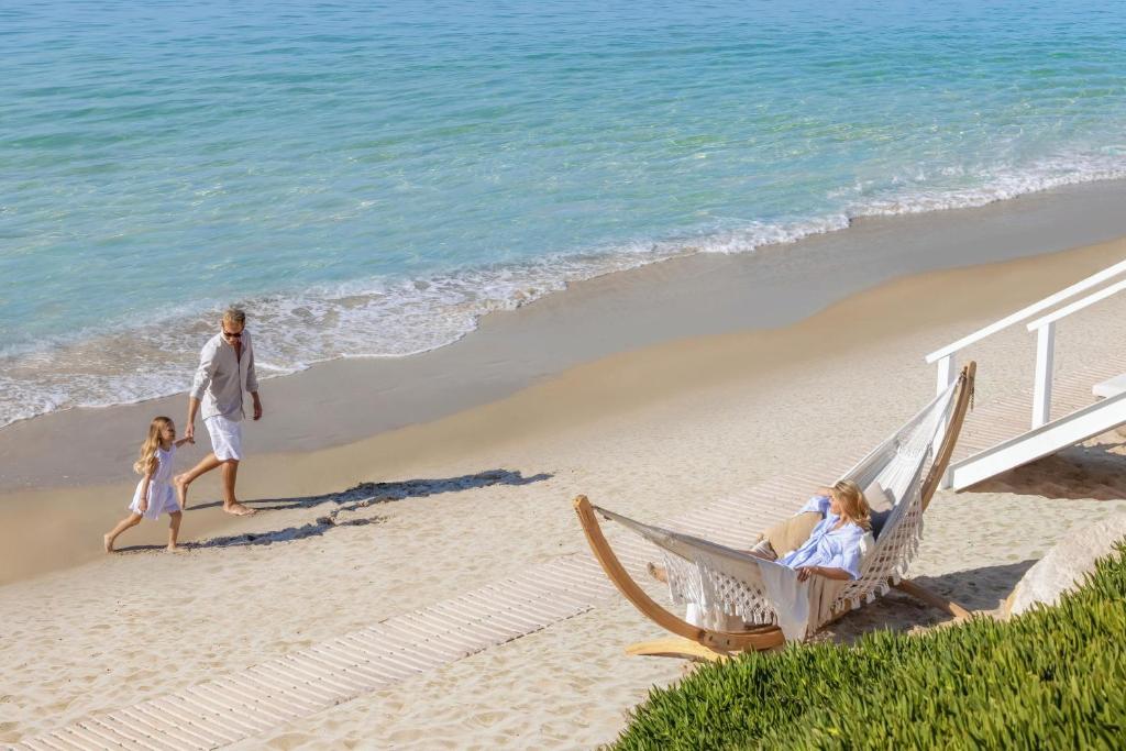 Ģimenes brīvdienas pludmalē, kur tētis pastaigājas ar meitu, kamēr māte atpūšas šūpuļtīklā. Skaista pludmales ainava ar mierīgu ūdeni un smiltīm.