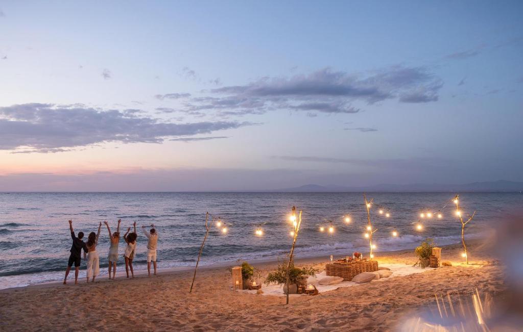 Pludmalē pie saulrieta grupa cilvēku svin brīvdienas, izstiepjot rokas gaisā. Apkārt ir romantiski izkārtota vieta ar gaismiņām un dekorācijām.