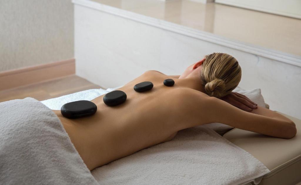 Mājas atmosfērā relaksējošs masāžas process ar karstām akmeņiem uz muguras.