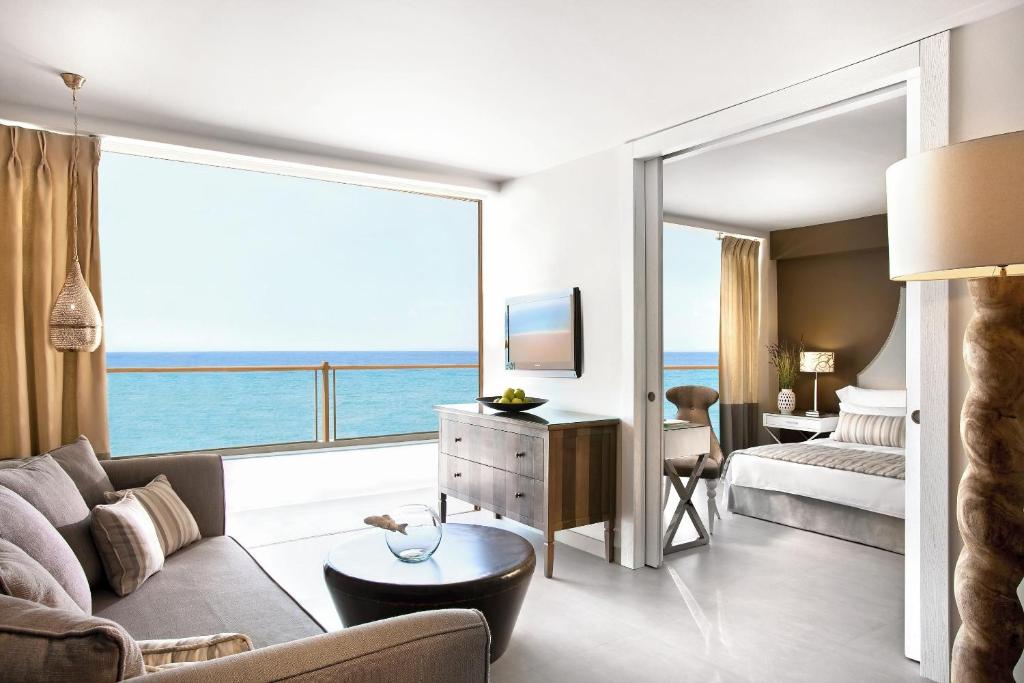 Mūsdienīga viesnīcas istaba ar skatu uz jūru, iekārtota ar komfortablu dīvānu, televizoru un elegantām mēbelēm. Gaismas un telpas izjūta rada relaksējošu atmosfēru.