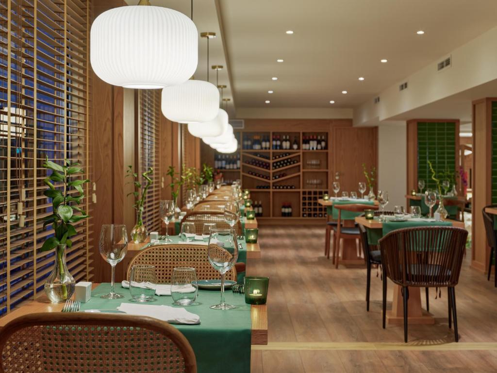 Moderns restorāns ar elegantiem galdiem, zaļiem galdautiem un izsmalcinātu apgaismojumu. Interjerā redzami koka elementi un glīti izkārtoti vīna plaukti.