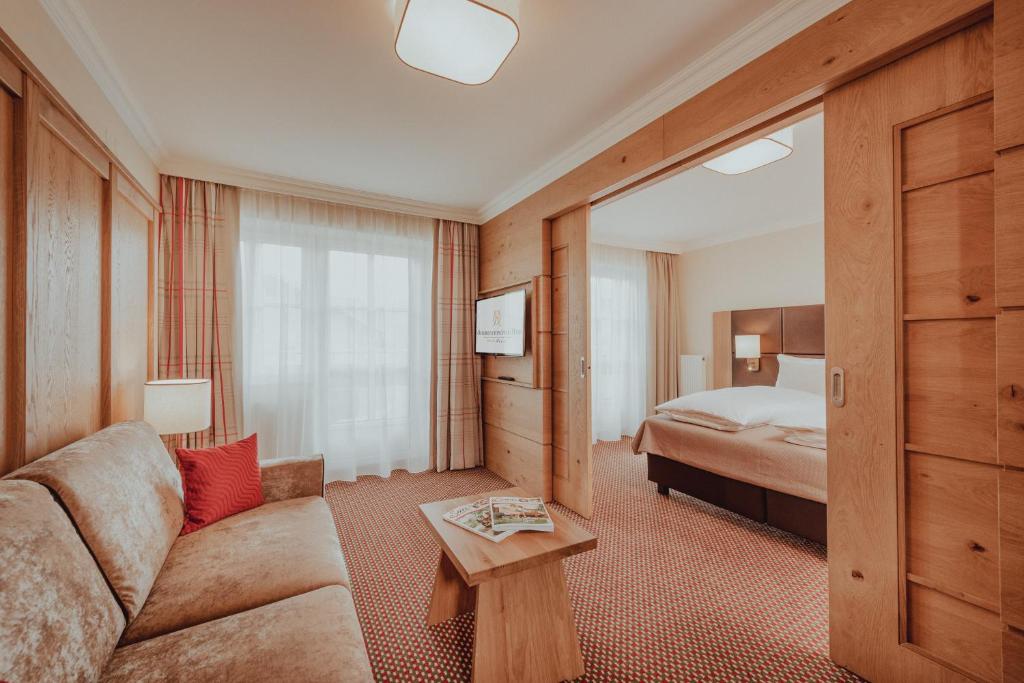 Mūsdienīgs viesnīcas numurs ar koka apdari, ērtu dīvānu un televizoru. Telpa ir gaiša, ar plašiem logiem un siltām krāsām, radot mājīgu atmosfēru.