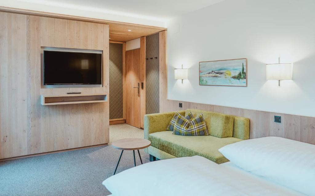 Mūsdienīgs viesnīcas numurs ar koka apdari, dīvānu un televizoru pie sienas. Telpā ir silta apgaismojuma un mākslas darbs, kas piešķir patīkamu atmosfēru.
