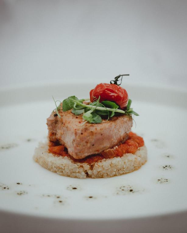 Gards un elegants ēdiens, kurā ir cepta zivs ar tomātu un zaļumiem, pasniegts uz kvinojas pamatnes.