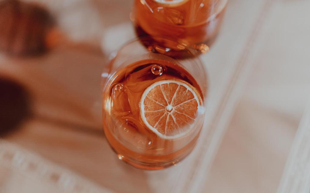 Salds dzēriens ar citrona šķēli, pasniegts glāzē, uz koka virsmas. Dzēriens ir dzidrs, ar gaismas atspīdumiem.