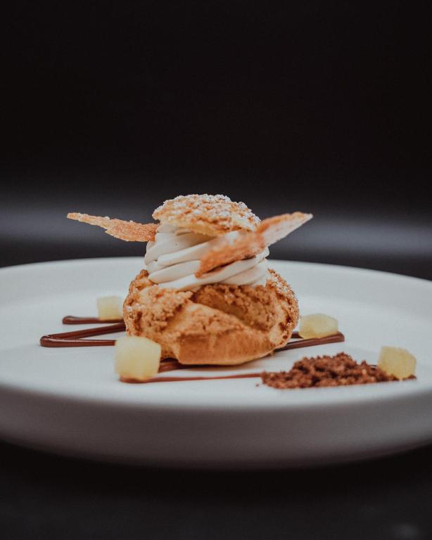 Elegants deserts ar krēmīgu pildījumu, dekorēts ar kraukšķīgām lapām un šokolādes mērci. Uz šķīvja redzami arī augļu gabaliņi un šokolādes drupačas.