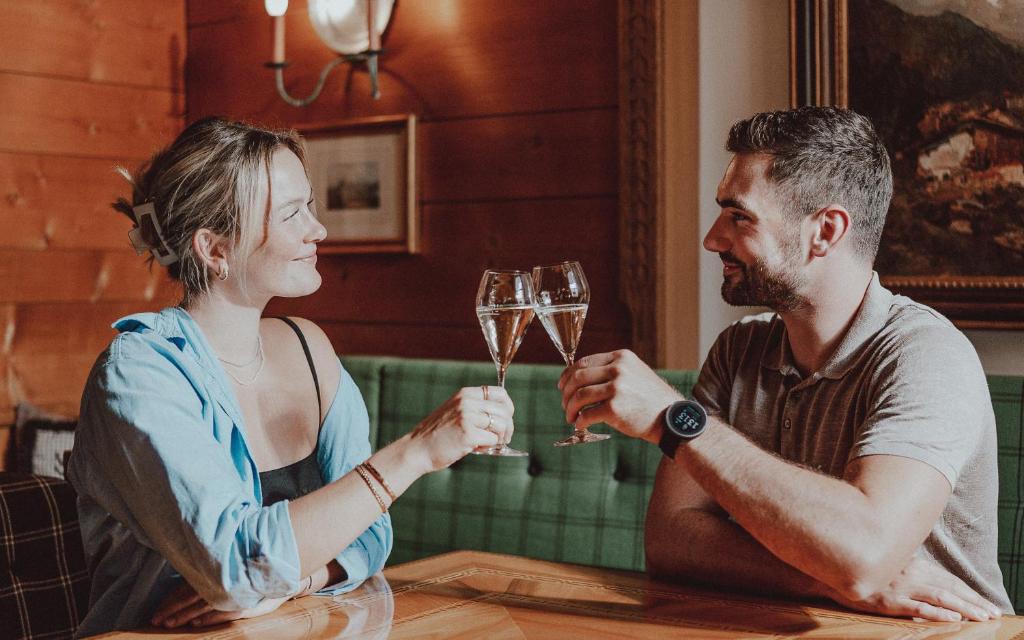 Pāris, svinot ar šampanieti, smaida un saskaras ar glāzēm kafejnīcā ar koka interjeru.