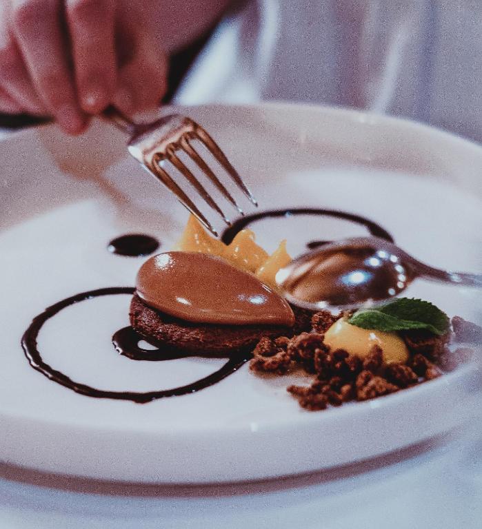 Gards deserts ar šokolādes krēmu, augļiem un kraukšķīgiem cepumiem uz balta šķīvja.