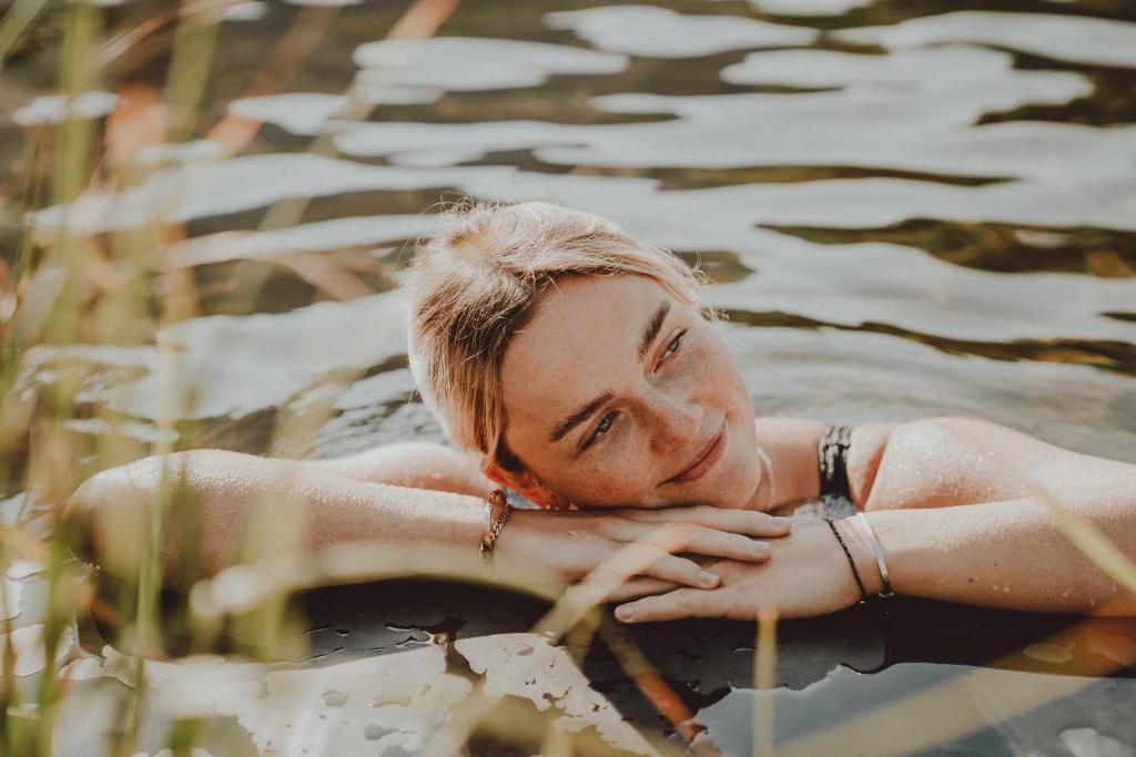 Sieviete, kas atpūšas ūdenī ar laimīgu izteiksmi, apņemot rokas ap krūtīm, apzaļumots fons.