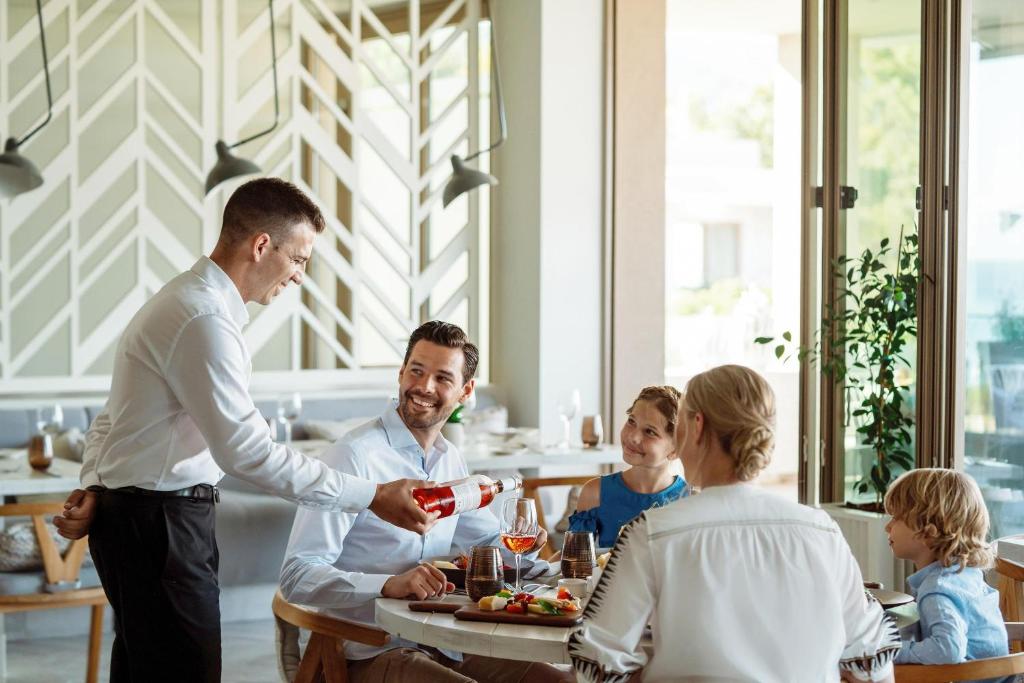 Ģimenes vakariņas modernā restorānā, apkalpojot viesus ar dzērieniem. Smaids un patīkama atmosfēra rada siltu un viesmīlīgu pieredzi.