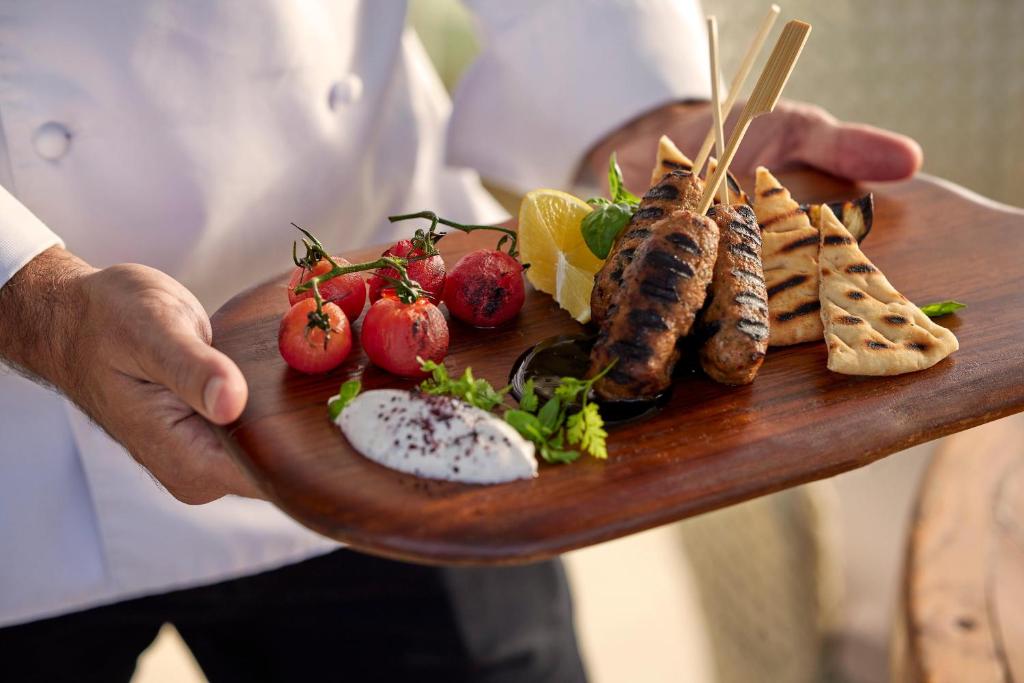 Grilēti kebabi ar tomātiem, svaigu zaļumu un jogurta mērci uz koka šķīvja.