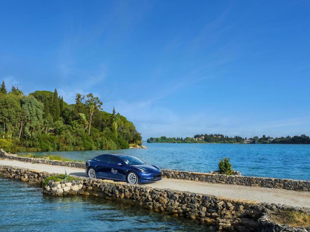 Elegants elektriskais automobilis pie ūdenskrātuves, apkārt gleznainām ainavām un zaļiem kokiem. Ideāla ainava ceļojumiem un atpūtai.