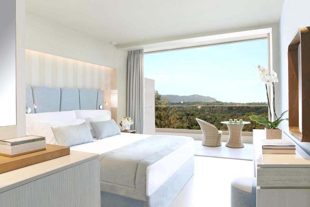 Mūsdienīga guļamistaba ar plašu skatu uz dabu, gaišām krāsām un minimālistisku dizainu. Telpā ir ērta gulta, viesistaba un dekoratīvas augu kompozīcijas.