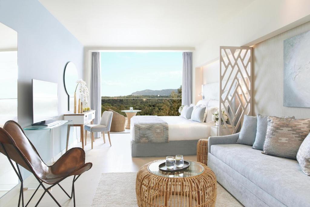 Mūsdienīgs viesnīcas numurs ar plašu skatu uz dabu, kurā ir ērts dīvāns, gultas zona un eleganti mēbeļu elementi. Interjers ir gaišs un stilīgs, radot relaksējošu atmosfēru.