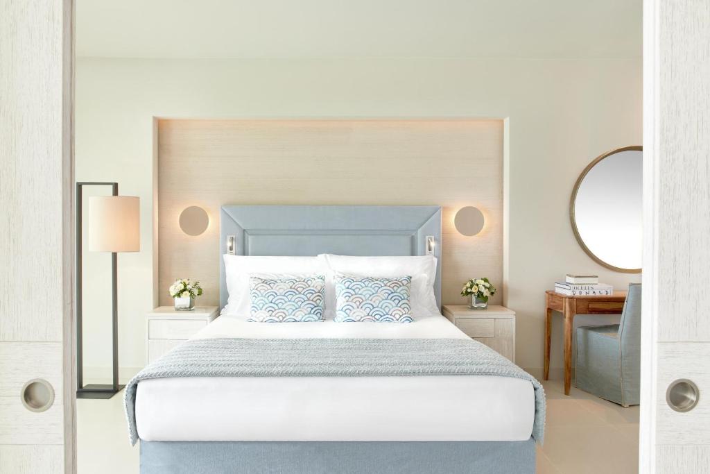 Mūsdienīgs guļamistabas interjers ar izsmalcinātu gultu, dekoratīvām spilvenēm un gaismas avotiem, radot relaksējošu atmosfēru. Sienu apdare un mēbeles piedāvā elegantu un komfortablu vidi.