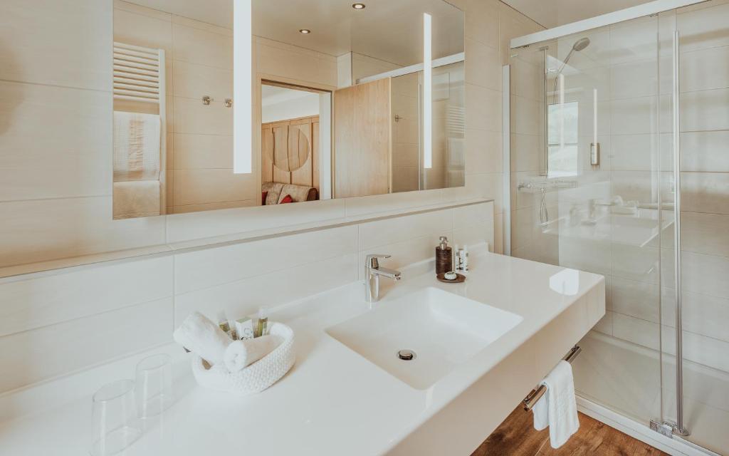 Moderns vannas istabas interjers ar gaišu izskatu, lielu spoguli un minimālistisku dizainu. Uz letes ir vannas piederumi un dvieļi, radot relaksējošu atmosfēru.