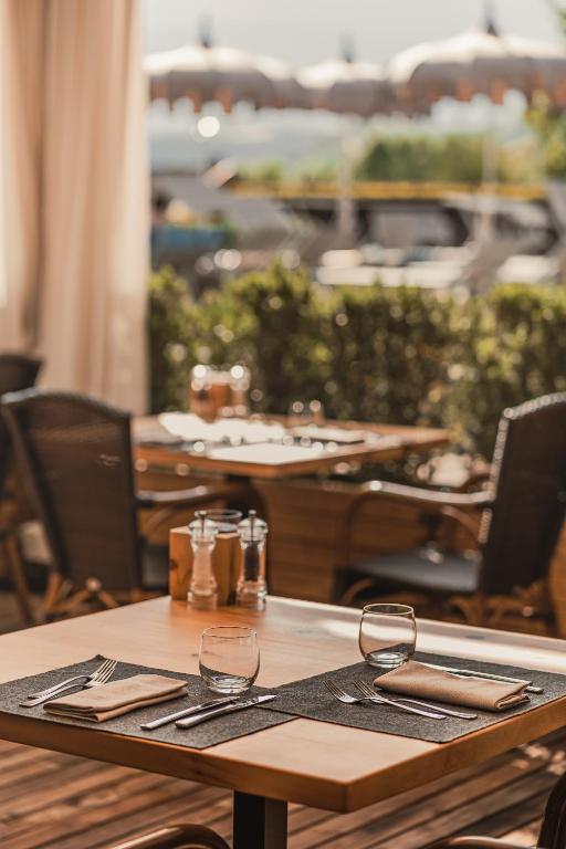 Elegantā restorāna galds ar galda piederumiem un glāzēm, fons ar dārzu un ēdināšanas zonu. Ideāla vieta relaksējošai maltītei.