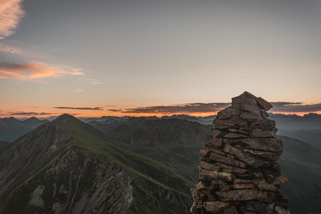 Kalnu ainava ar akmeņu krāvumu priekšplānā un krāšņu saulrietu debesīs.
