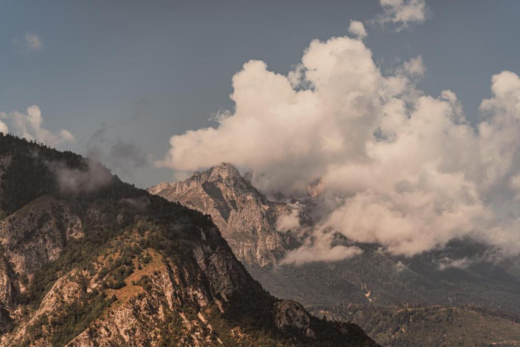 Kalnu ainava ar mākoņiem, kas pārklāj kalnu virsotnes, radot dramatiski skaistu skatu. Dabas ainava ar zaļām nogāzēm un klusiem mākoņiem.