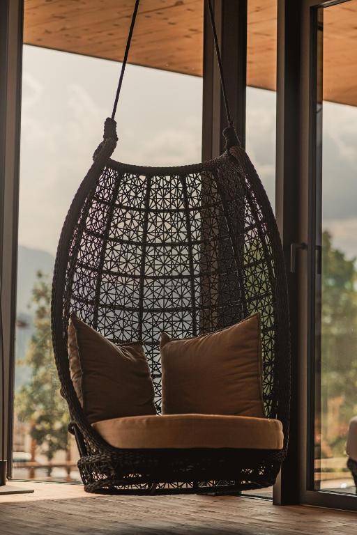 Mūsdienīgs šūpuļkrēsls ar mīkstiem spilveniem, kas karājas pie lieliem logiem ar skatu uz dabu. Ideāla vieta relaksācijai un atpūtai.