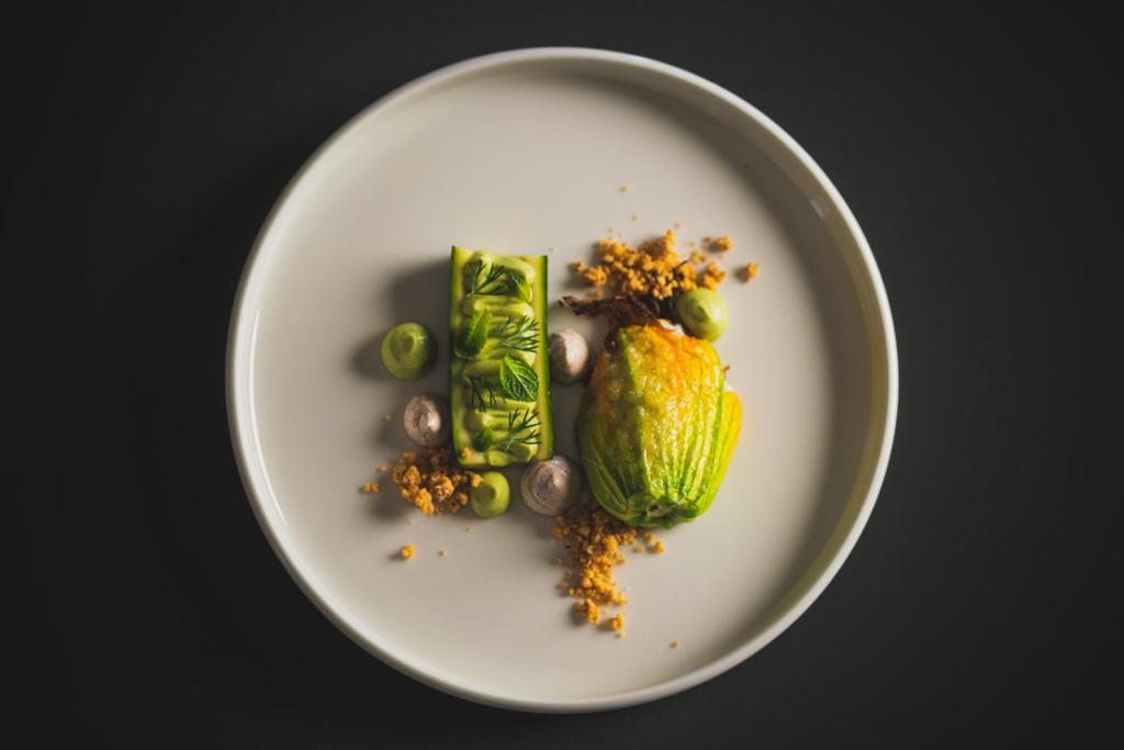 Gurķu un ziedkāpostu trauks ar zaļajiem augļiem un garšaugiem, pasniegts uz balta šķīvja.