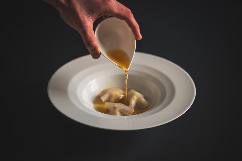 Siltā buljona pievienošana traukam ar daļēji redzamiem ēdieniem, uz melna fona.