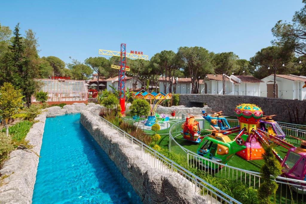 Krāsains atrakciju parks ar bērnu karuseļiem un zilo ūdens kanālu, ko ieskauj zaļa vide un koki. Ideāla vieta ģimenes izklaidei.