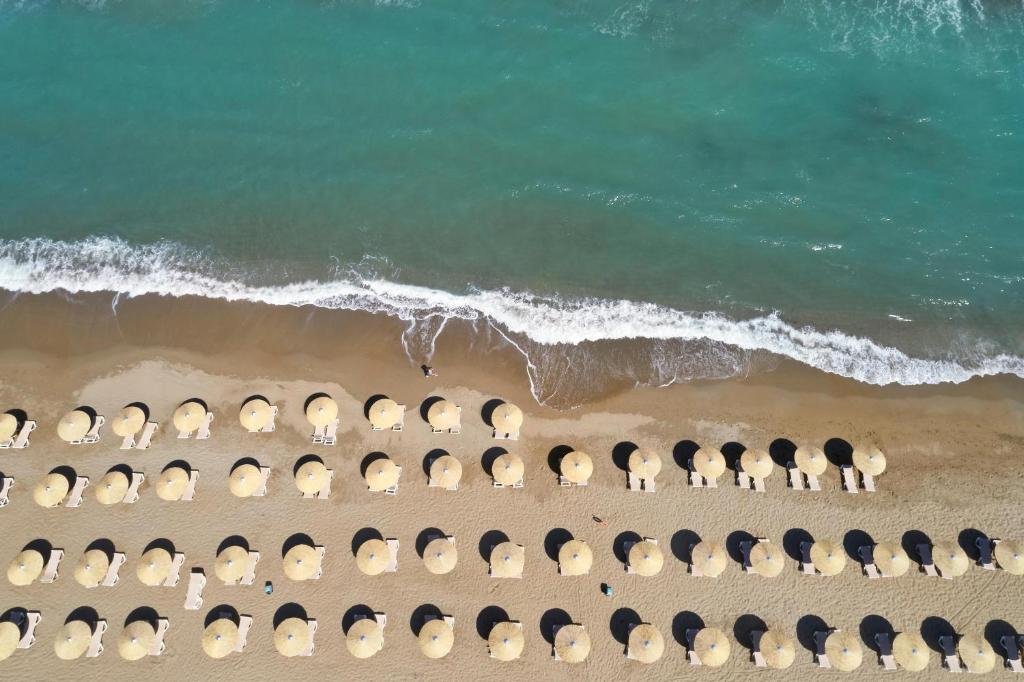 Pludmales ainava ar saulessargiem, kas sakārtoti gar smiltīm, un viļņiem, kas krīt pie krasta. Ūdens ir dzidrs un zils, radot relaksējošu atmosfēru.