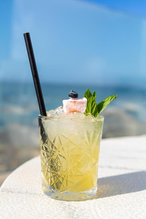 Atsvaidzinošs kokteilis ar piparmētru un ogām, pasniegts caurspīdīgā glāzē ar salmiņu. Fons veido jūras ainava ar zilu debesu atspulgu.